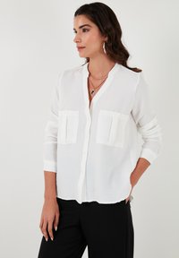 White button-up shirt with a mandarin collar, two chest pockets, long sleeves, and a lightweight, slightly textured fabric.