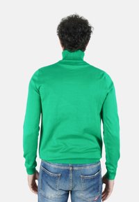 Maglione a collo alto verde realizzato in tessuto lavorato a maglia, con maniche lunghe e dettagli a costine su collo e orlo. Abbinato a jeans di denim blu.