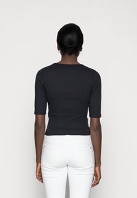 Černý, žebrovaný crop top s krátkými rukávy, jednoduchý design, kulatý výstřih. Sestaveno s bílými džíny, které zdůrazňují přiléhavý siluetu.