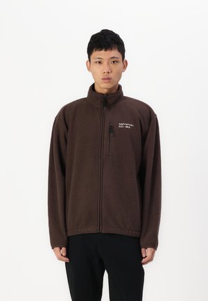 Braune Fleecejacke mit hohem Kragen und Reißverschluss. Verfügt über eine Brusttasche mit Reißverschluss und ein gesticktes Logo auf der linken Seite.