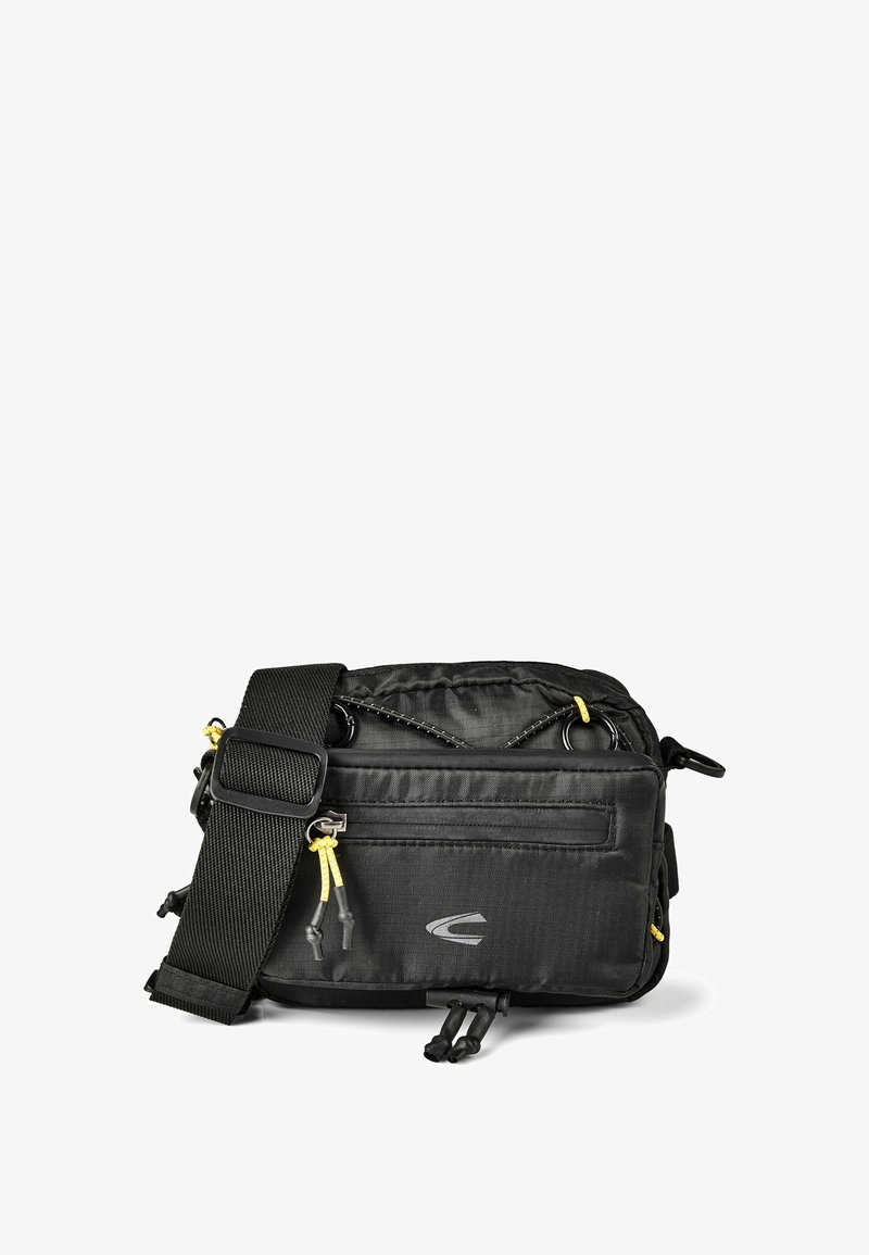Petit sac bandoulière noir compact avec sangle large réglable, poche zippée à l'avant, détail en corde élastique et tirettes de fermeture éclair jaunes, sur fond blanc.
