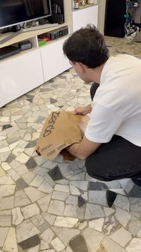 Brašna iz rjavega kraft papirja z napisem "Zalando" natisnjenim v črni barvi, ki jo drži oseba, ki kleči na vzorčastem kamenem tleh.