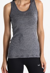 Canottiera sportiva grigia senza maniche con una sottile consistenza melangiata, design aderente e dettaglio del logo vicino al colletto. Abbinata a leggings neri.