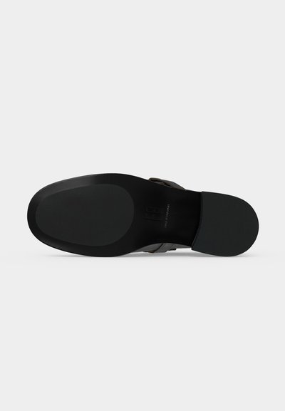 Semelle d'une chaussure en cuir noir avec un bout lisse et arrondi et un talon légèrement surélevé sur un fond clair uni.