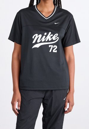 Personne portant une tenue de sport noire Nike, comprenant un t-shirt à manches courtes avec le texte "nike 72" et un pantalon assorti avec un logo Nike blanc.
