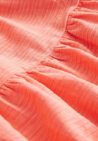 Gros plan sur un tissu rose corail doux avec un subtil côtes verticales et un détail de couture froncée.