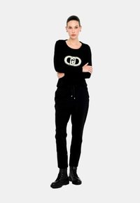 Maglione nero a maniche lunghe con scollatura rotonda e un design con logo metallico. Abbinato a pantaloni neri e stivali da combattimento con lacci.