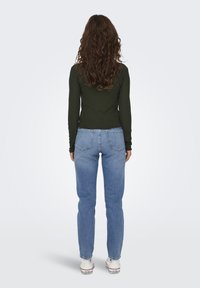 Grön ribbade långärmad topp som är i kombination med ljusblå raka jeans och vita sneakers, sedd bakifrån.