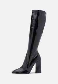 Bottes noires montant jusqu'aux genoux avec une finition vernie brillante, bout carré et talon haut épais, affichant une silhouette élégante et ajustée.