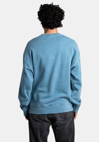 Světle modrý sweatshirt s uvolněným střihem, žebrovanými manžetami a lemem a měkkou texturou. Obsahuje snížené švy na ramenou a jednoduchý design.