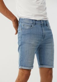 Shorts en denim bleu avec revers, présentant un design classique à cinq poches, un bouton en métal et une légère décoloration du tissu.