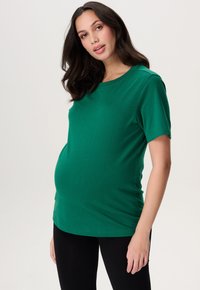 Groene zwangerschaps T-shirt met korte mouwen, gemaakt van zachte katoen. Heeft een ronde halslijn en een ontspannen pasvorm die ruimte biedt voor een groeiende buik.