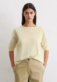 Maglione leggero giallo chiaro, dal taglio rilassato, con maniche lunghe e scollatura a girocollo, abbinato a pantaloni beige con tasche frontali.