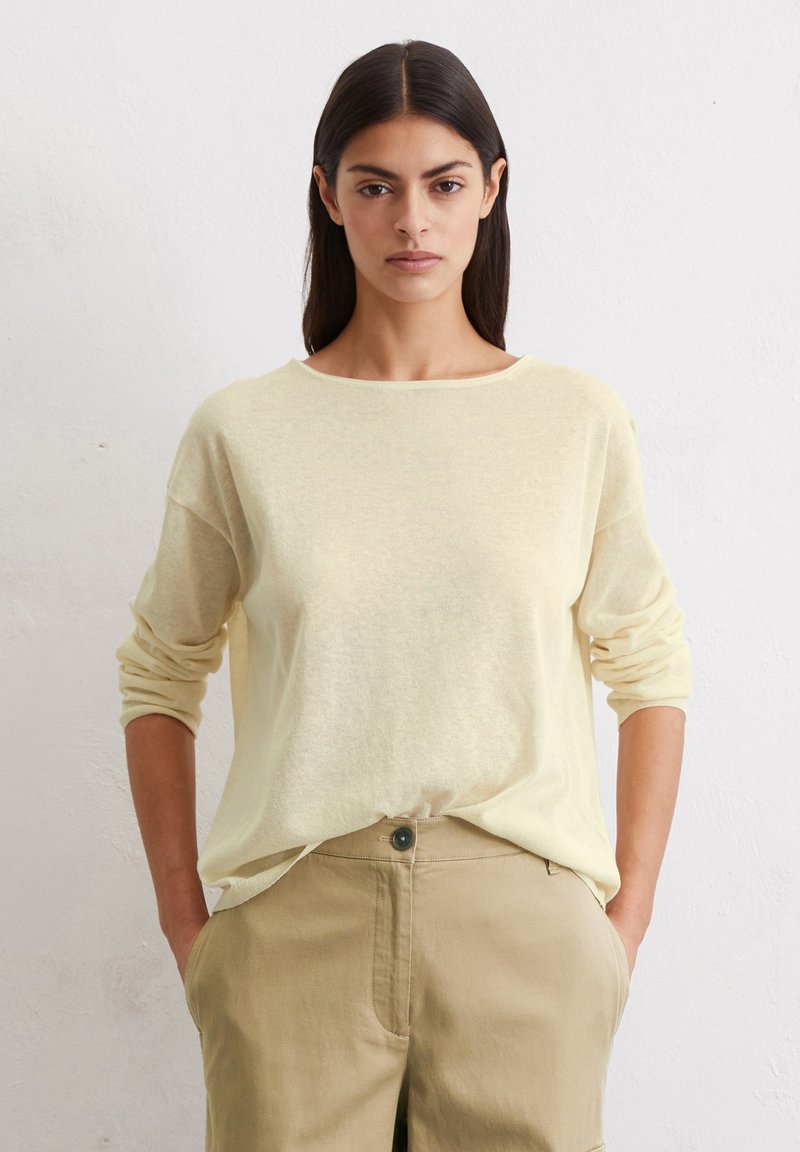 Maglione leggero giallo chiaro, dal taglio rilassato, con maniche lunghe e scollatura a girocollo, abbinato a pantaloni beige con tasche frontali.