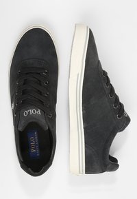 Mörkgrå mockaskor med svarta snören, vit gummisula och logotypdetalj. Har en ren design och kontrasterande randiga detaljer.