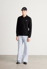 Črna polo majica z dolgimi rokavi, svetlo modre široke kavbojke, črna kapa z logotipom in črni čevlji. Preprost in priložnosten dizajn z kontrastnimi barvami.