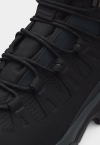 Κοντινό πλάνο μαύρου ορειβατικού μποτάκου με σταυρωτά στρογγυλά κορδόνια, επενδεδυμένη γλώσσα και υφασμένο, ραμμένο συνθετικό πάνω μέρος.