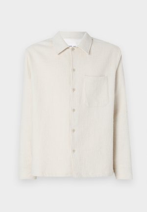 Krémová košile na knoflíky vyrobená z texturované látky, s límcem, dlouhými rukávy a jednou náprsní kapsou.