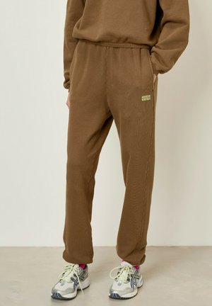Bruine joggingbroek van zacht materiaal, met een elastische tailleband en zijzakken. Klein groen logo-accent op de linkerdij.