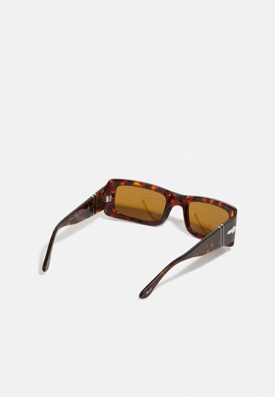 Óculos de sol em tartaruga castanha com armação quadrada, lentes castanhas e acabamentos em prata nas hastes. Textura de plástico suave em toda a peça.