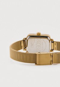 Ρολόι με χρυστό πλέγμα στο λουρί, τετράγωνη κάσα, μεταλλική πίσω όψη και περιστροφικό κουμπί. Το λουρί έχει υφασμένο ανάγλυφο σχέδιο.