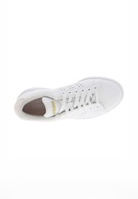 Zapatilla blanca con parte superior de cuero liso, salpicada de pequeñas perforaciones, detalles texturizados en el talón y cordones planos. Detalle del logo en dorado.