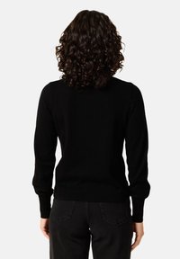 Mustat neuleet pitkillä hihoilla, pyöreällä kauluksella ja ribbaamalla viimeistelyllä. Pehmeä rakenne, istuva muotoilu. Yhdistetty mustiin housuihin, mikä korostaa sujuvaa siluettia.