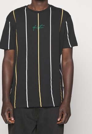 Persona que lleva una camiseta negra con rayas verticales amarillas y blancas y texto verde "Tu turno" centrado en el pecho.