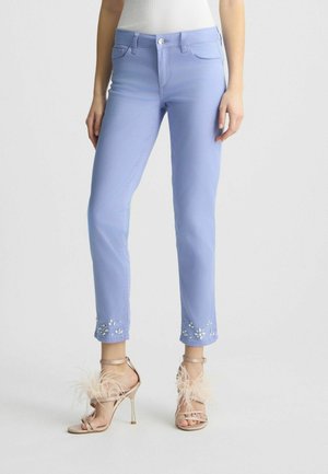 Light blue denim jeans feature floral bead embroidery at the hem. Paired with nude high-heeled sandals adorned with feathers.