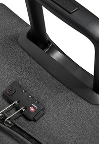 Mustan kankaan pyörällinen laukku, jossa on vedettävä kahva, yhdistelmälukko ja hopeiset vetoketjun vedin turvallisuuden ja pääsyn mahdollistamiseksi.