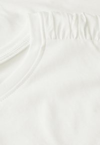 Camiseta de algodón blanca con un escote fruncido, textura suave y acabado liso, con una vista en primer plano que resalta los detalles de la costura.