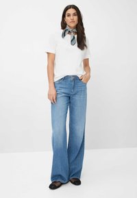 Witte top met korte mouwen, gecombineerd met een zwart-wit patroon sjaal, en wijde blauwe spijkerbroek en zwarte mesh flats. Eenvoudig en casual ontwerp.