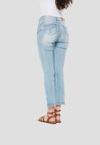 Lichtblauwe denim jeans met een cropped lengte, voorzien van achterzakken en decoratieve stiksels. Gecombineerd met bruine sandalen met bandjes.