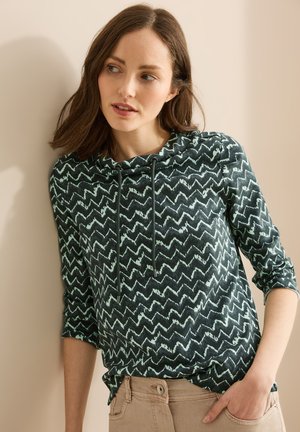 Pull à capuche vert foncé avec un motif en zigzag menthe. Il a un cordon de serrage et des manches trois-quarts, fabriqué en tissu doux.
