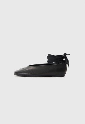 Ballerines en cuir noir avec un bout pointu, dotées d'un lien à la cheville en tissu tissé et d'un petit accent décoratif sur le bout.