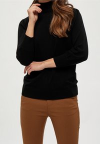 Svart polotröja med ribbade muddar och fåll, kombinerad med bruna åtsittande byxor. Tyget verkar slätt och något stretchigt.