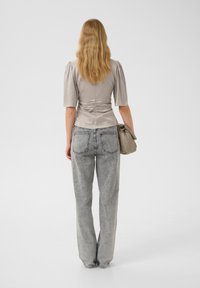 Light gray fitted top with puff sleeves and a ruched waist, paired with high-waisted, wide-leg faded jeans. Textured material, neutral tones.