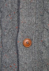 Szary dzianinowy kardigan z wzorami w warkocz, pomarańczowymi i niebieskimi plamkami oraz okrągłym brązowym guzikiem z czterema dziurkami.