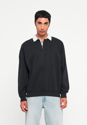 Black sweatshirt with a white collared neckline, two-button placket, and ribbed cuffs, paired with light blue jeans. Casual design, soft texture.