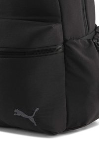 Sac à dos noir en tissu résistant, doté d'une poche zippée et d'un logo gris discret. Forme courbée avec des sections rembourrées pour le confort.