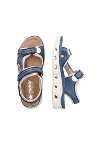 Blå syntetiska sandaler med en vadderad tan-färgad sula, kardborreband och utskärningar för ventilation. Sålen är texturerad med dräneringshål.