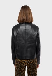 Black leather jacket with a smooth texture, cropped design, and minimalistic collar. Paired with leopard print pants featuring pockets.