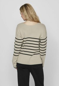 Pullover beige con strisce orizzontali nere, polsini a coste e scollatura ampia. Il tessuto sembra morbido con una vestibilità comoda.