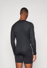 Schwarzes, langärmeliges Sportshirt aus strukturiertem Stoff, mit figurbetontem Design und kontrastierenden Nähten, kombiniert mit schwarzen, figurbetonten Shorts.