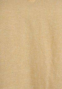 Textura de tela de lino beige con patrón de tejido visible y pliegues sutiles, mostrando fibras naturales y un acabado mate suave.