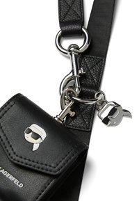 Black faux leather crossbody bag with a textured finish, featuring silver hardware, a key charm, and a graphic logo on the front.