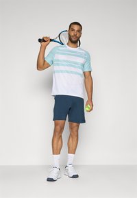 Conjunto deportivo que incluye una camiseta de rayas azul clara y blanca de manga corta, pantalones cortos navy y zapatillas deportivas blancas. Sosteniendo una raqueta de tenis y una pelota.