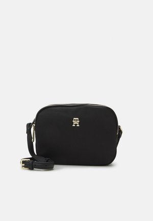 Svart crossbody veske laget av stoff med en glatt tekstur, som har et gullfarget logo, glidelås-lukking og justerbar stropp.
