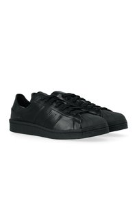 Un paio di sneakers in pelle nere a punta bassa con punte testurizzate e lacci neri su uno sfondo bianco.
