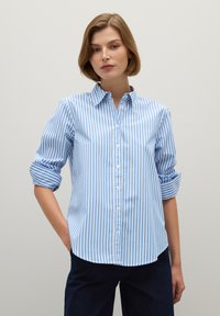 Chemise à rayures bleues et blanches avec un col, des manches retroussées et un ourlet arrondi. Fabriquée en tissu avec une texture lisse.